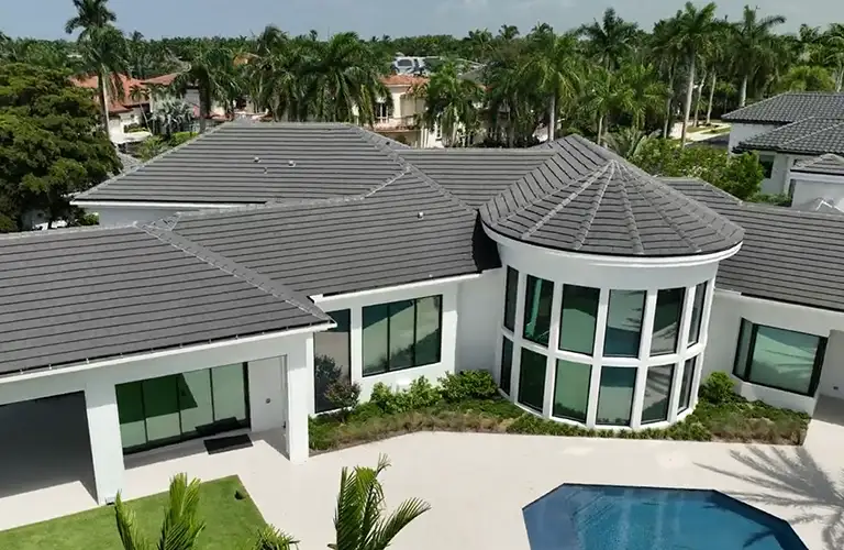 florida-window-replacement Aerial view of a modern single-story house with gray tiled roofs, a curved glass-front section, and a blue rectangular pool in the yard.